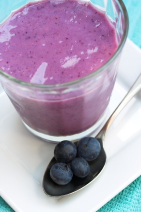 Blueberry smoothie sitting on plate next to raw blueberries