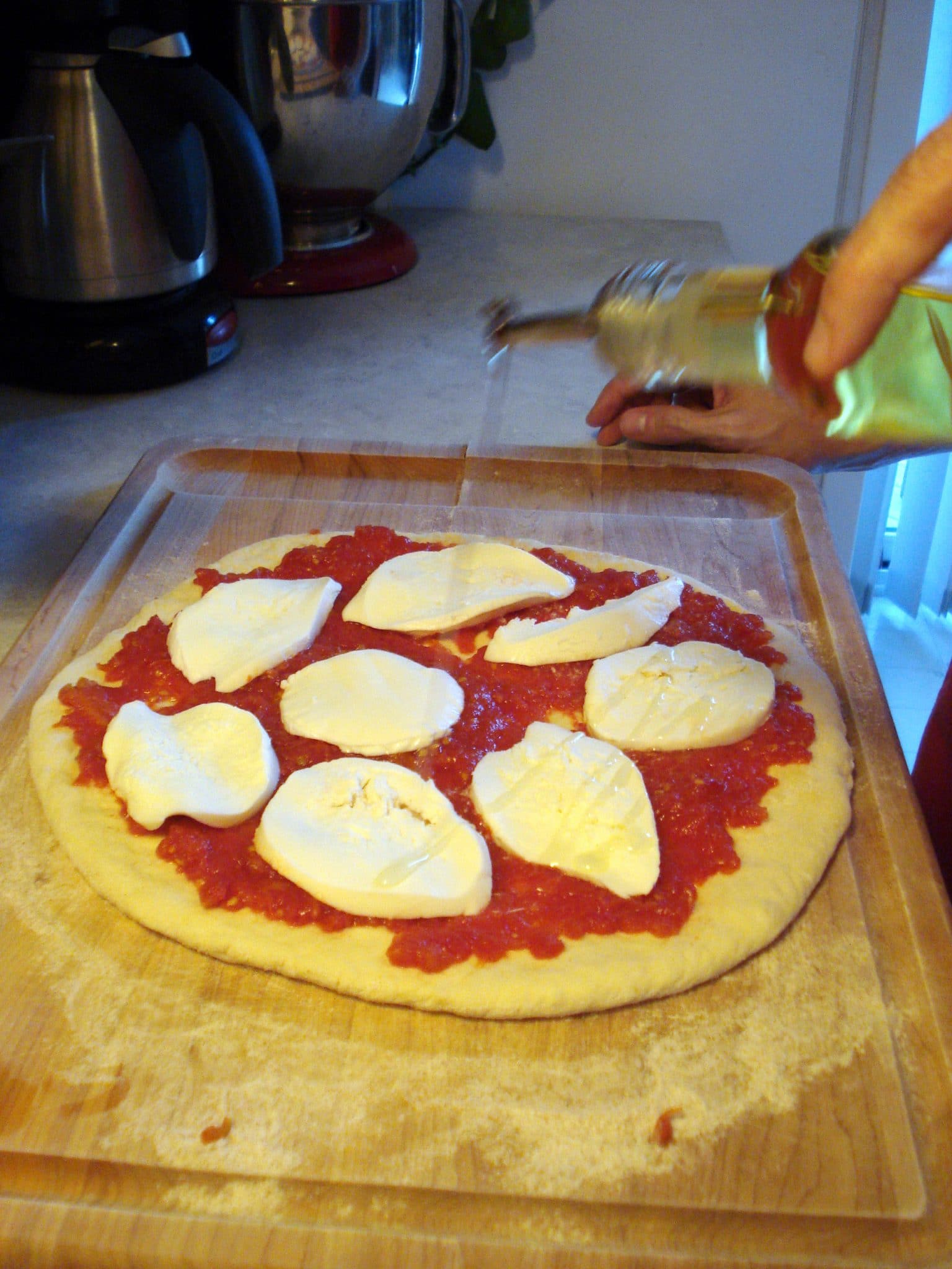 Uncooked pizza, receiving a drizzle of olive oil