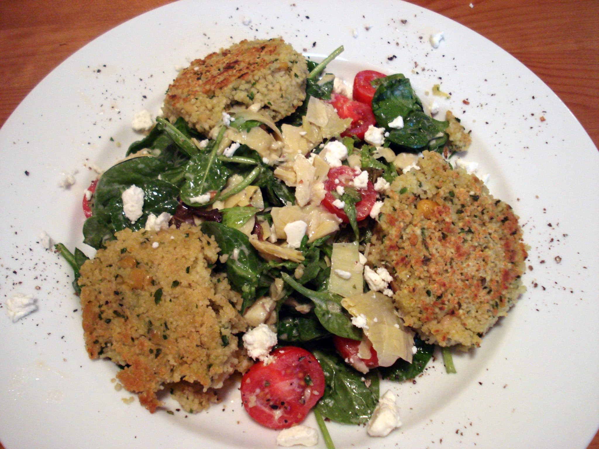 Plate of couscous cakes on top of baby spinach and tomato salad