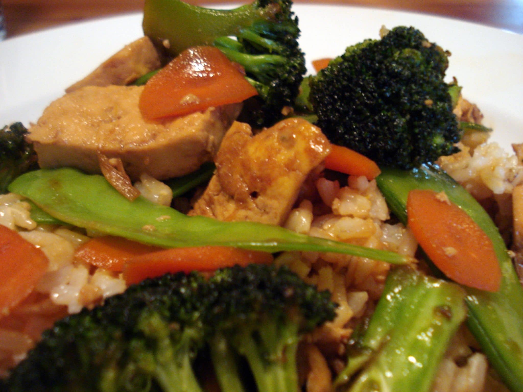 Close up of asian stir-fry; broccoli, snap peas, red pepper, and tempeh over rice