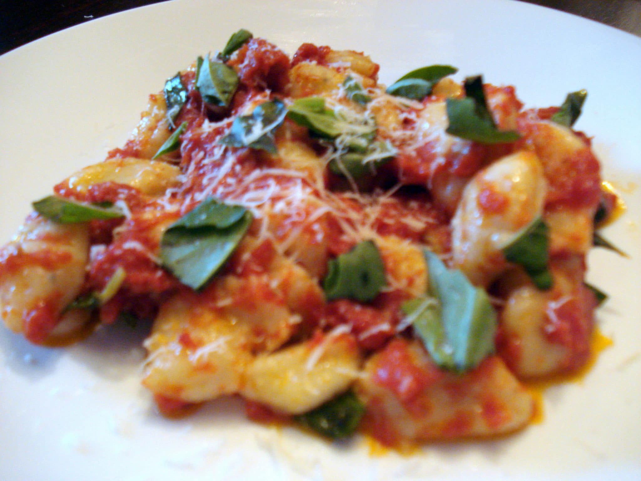 Gnocchi on plate covered in marinara sauce and fresh basil