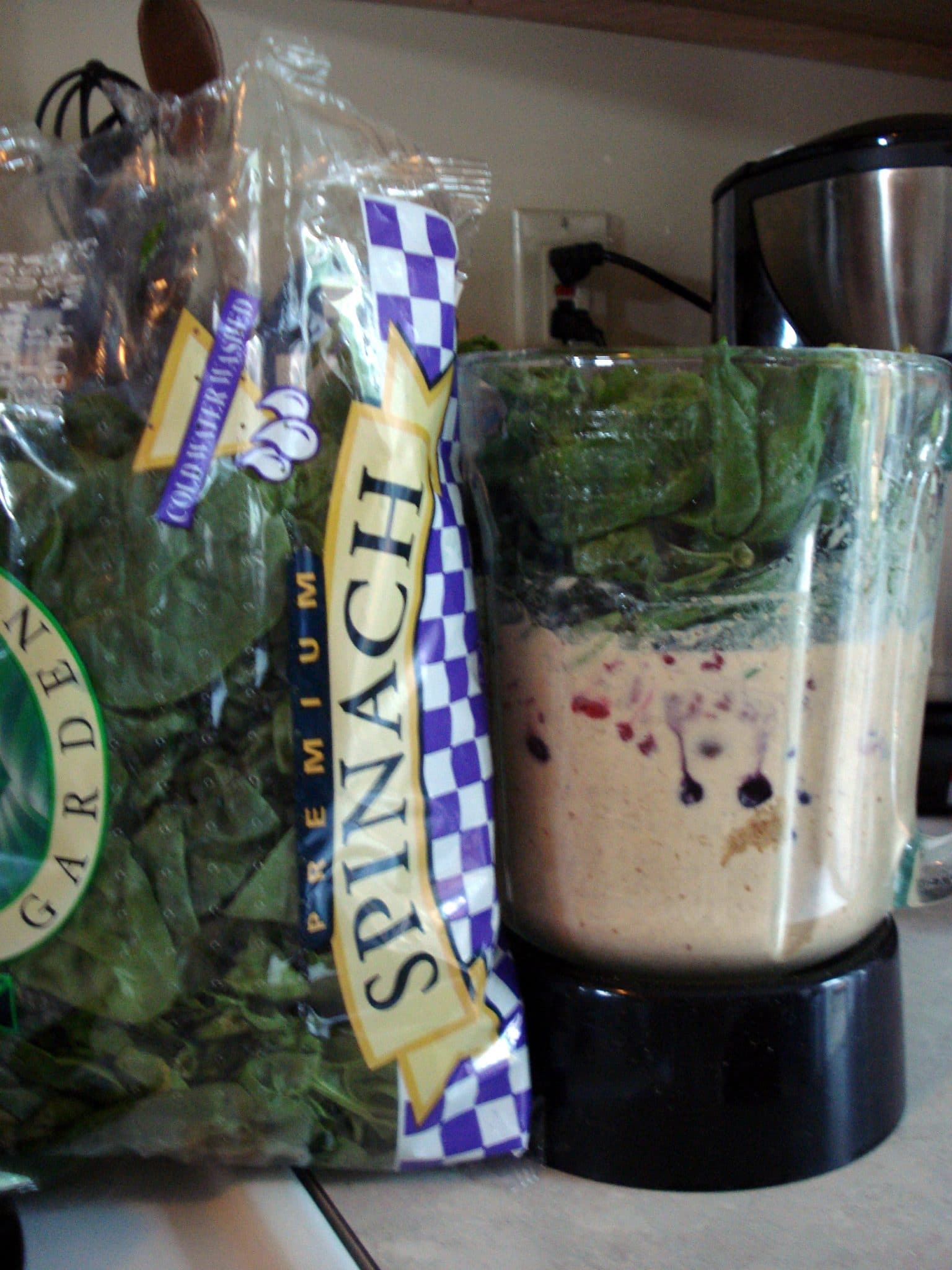 Bag of spinach next to blendr of smoothie