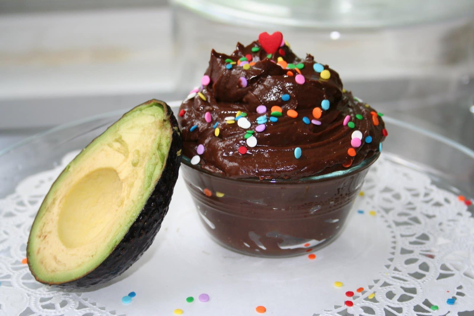 Small ramekin of avocado mousse with colorful sprinkles with half an avocado sitting on plate