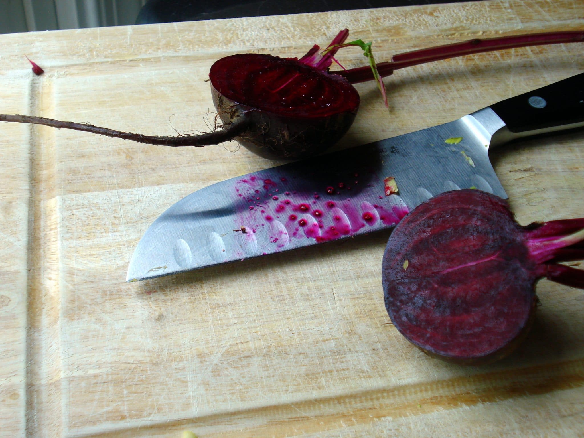 One beet cut in half on cutting board with knife
