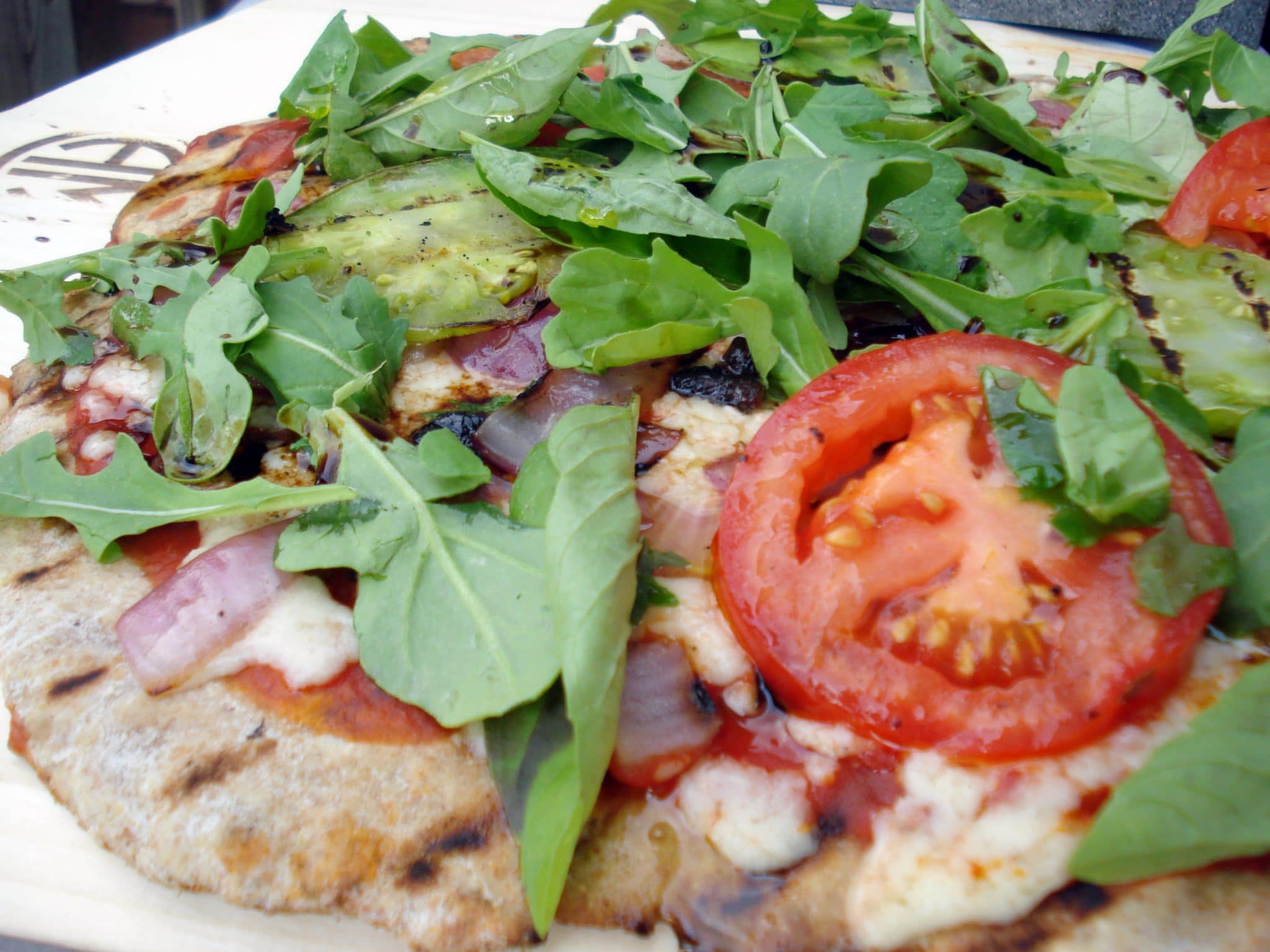 Close up of homemade grilled pizza covered in leafy greens and tomatoes