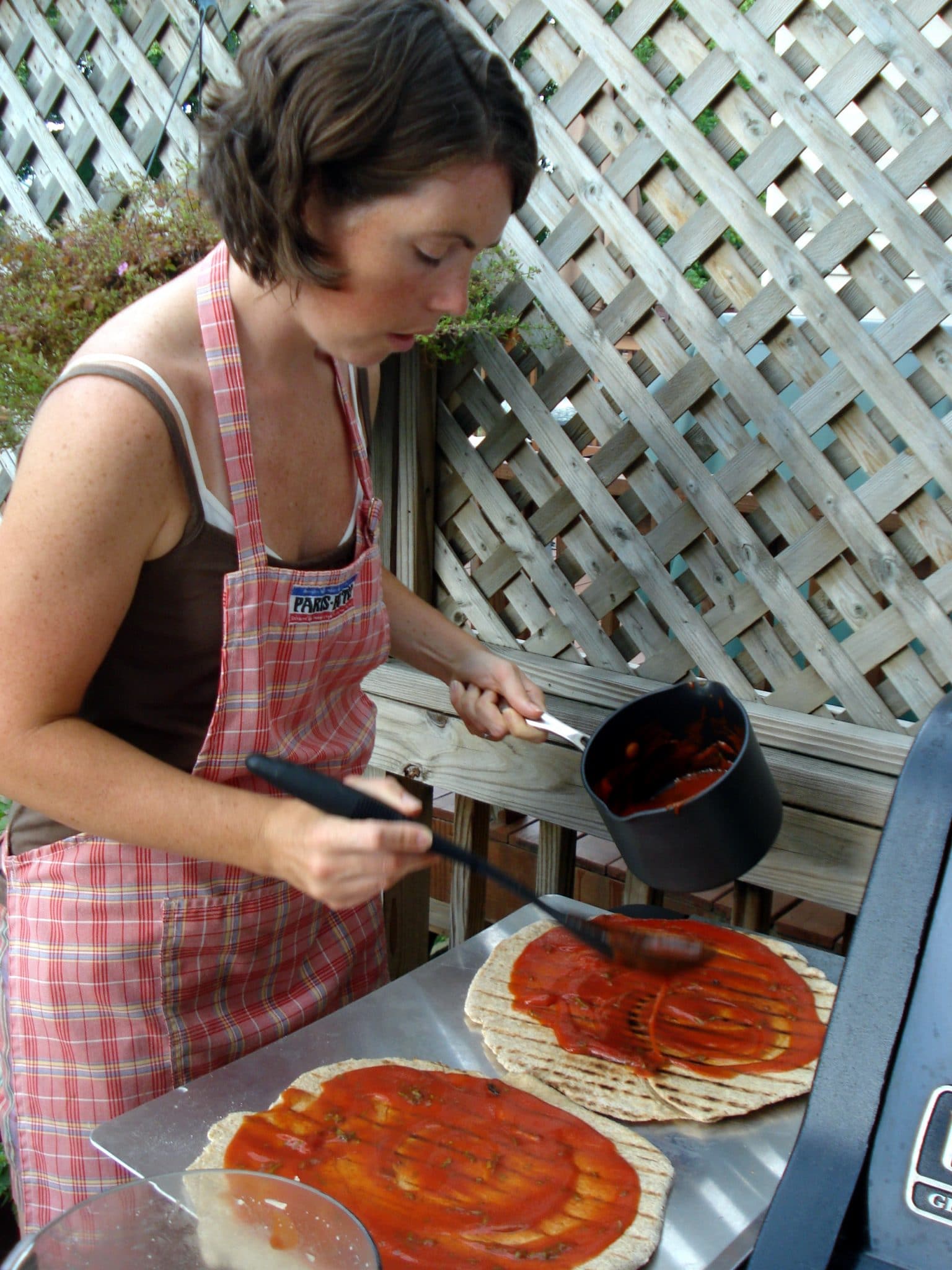 Erin saucing pizzas for grilling