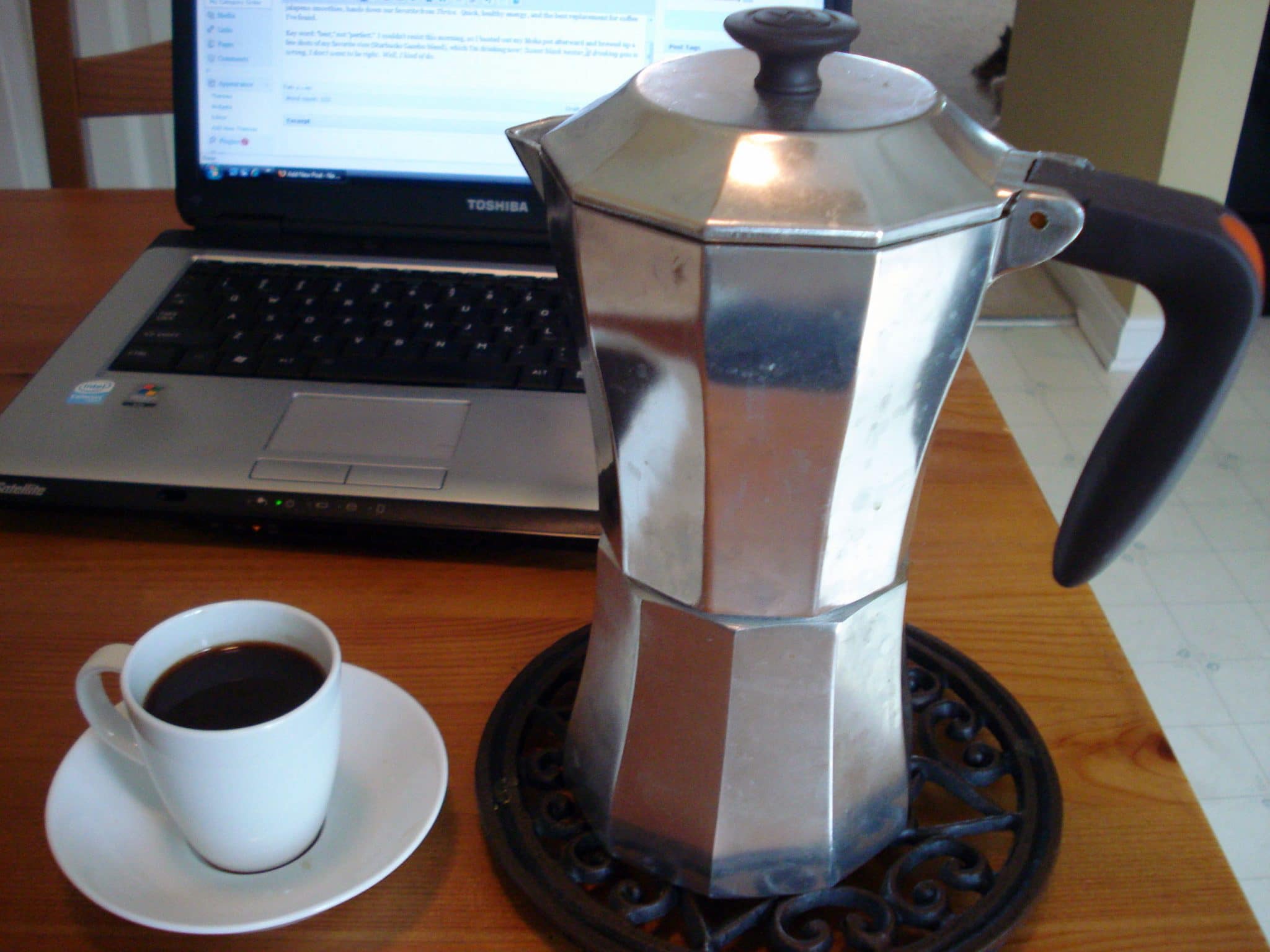 Moka pot and cup of coffee on table in front of laptop