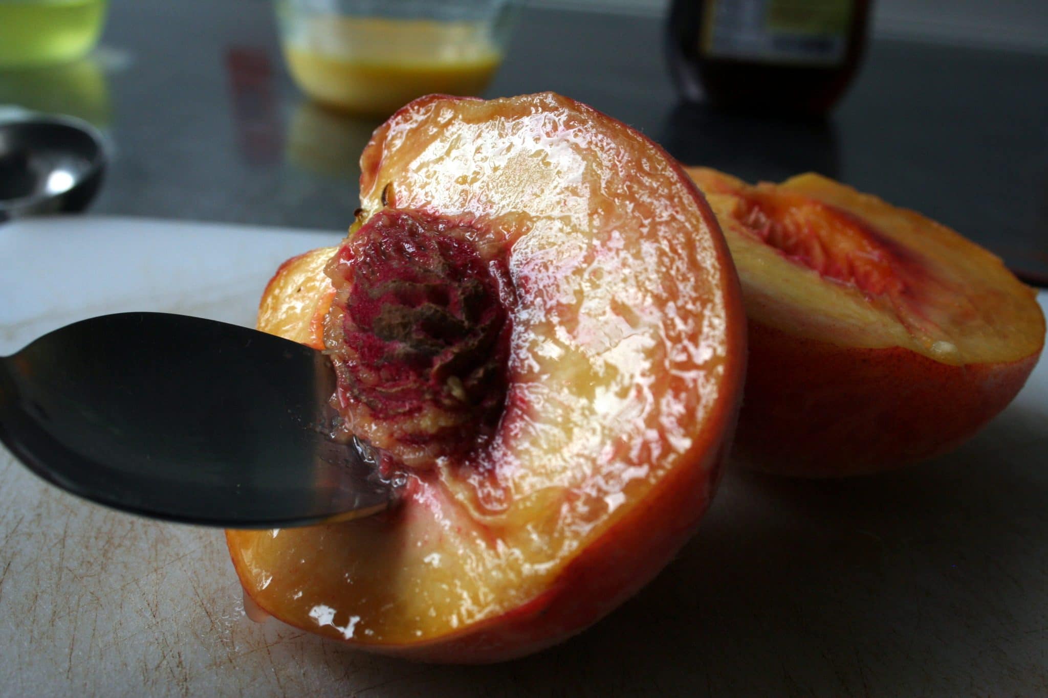 Spoon scooping pit out of peaches