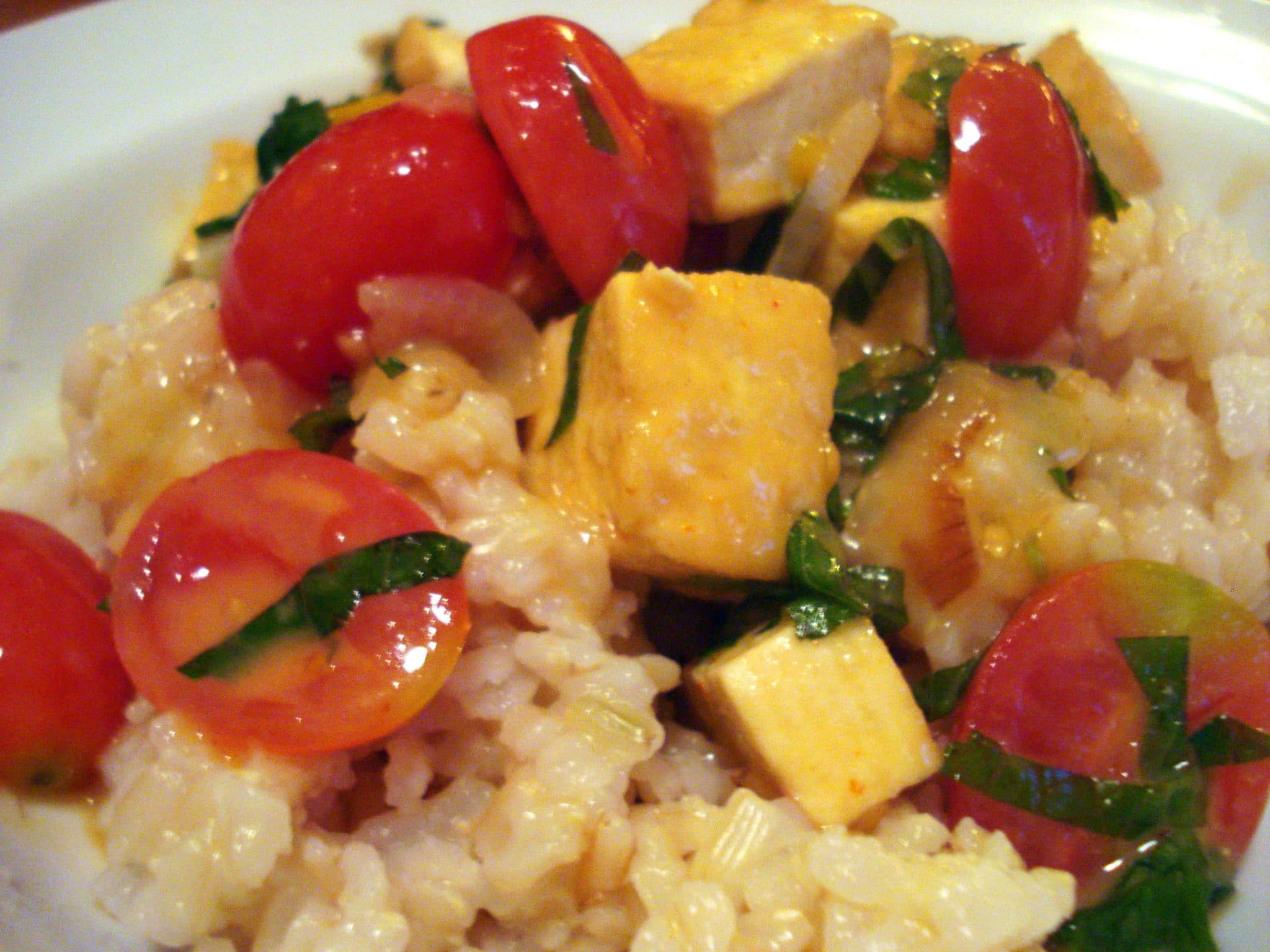Close up of tofu with tomatoes on top of rice with fresh basil