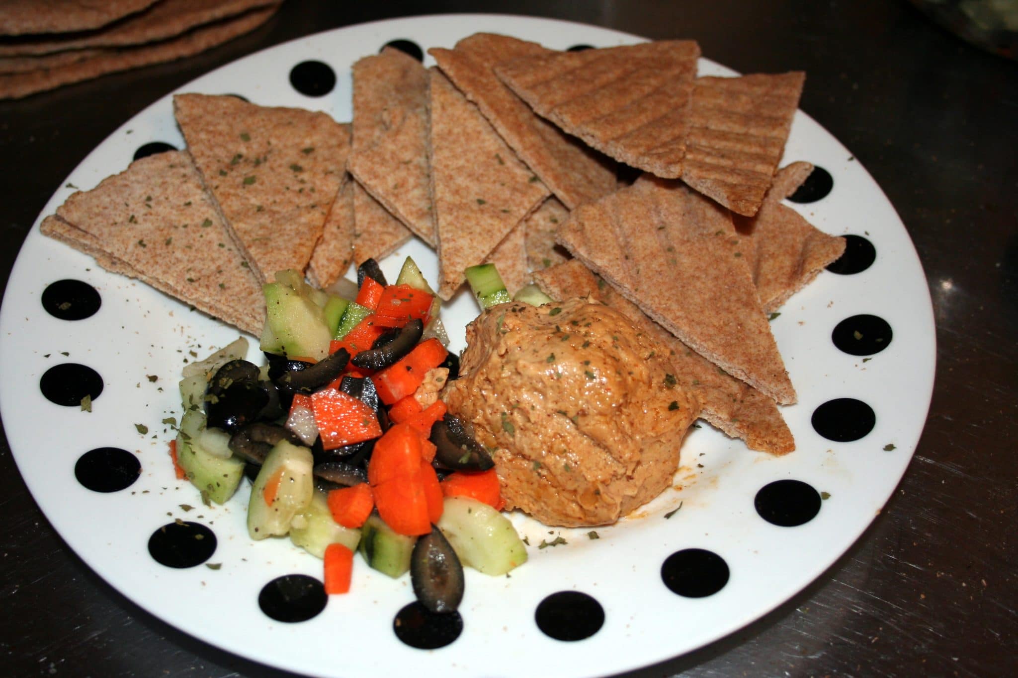 Vegan flatbread cut into triangles on plate with carrots, olives and zucchini