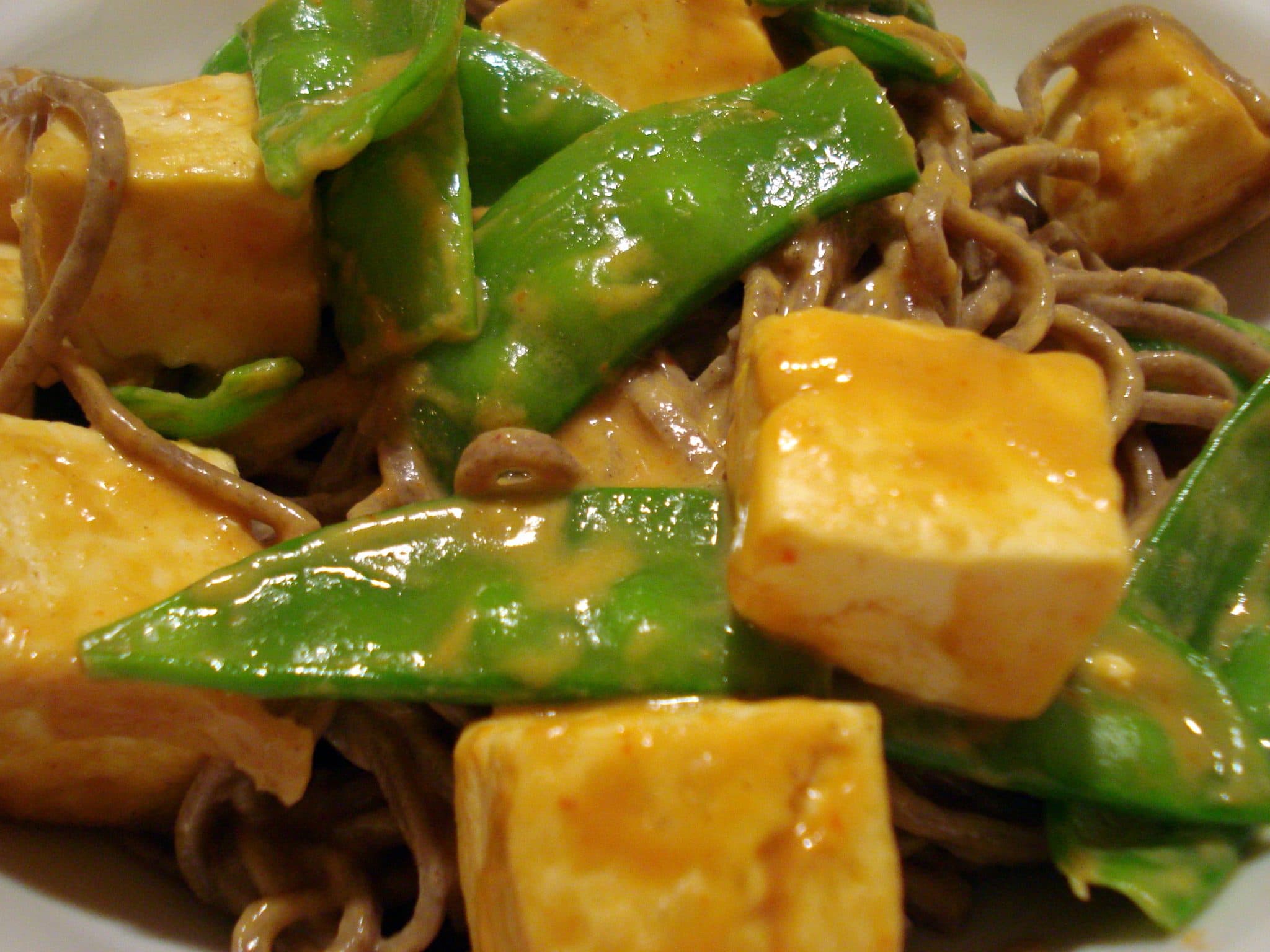 Close up of Peanut Butter Tofu with Snow Peas on top of Soba noodles
