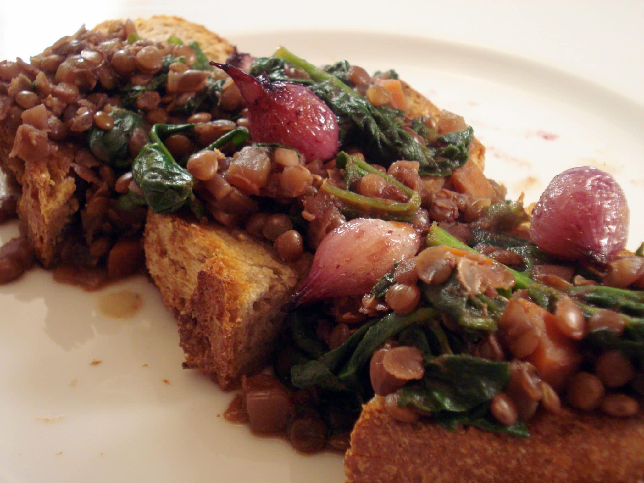 Plate of Wine Braised Lentils over toast with spinach and red pearl onions