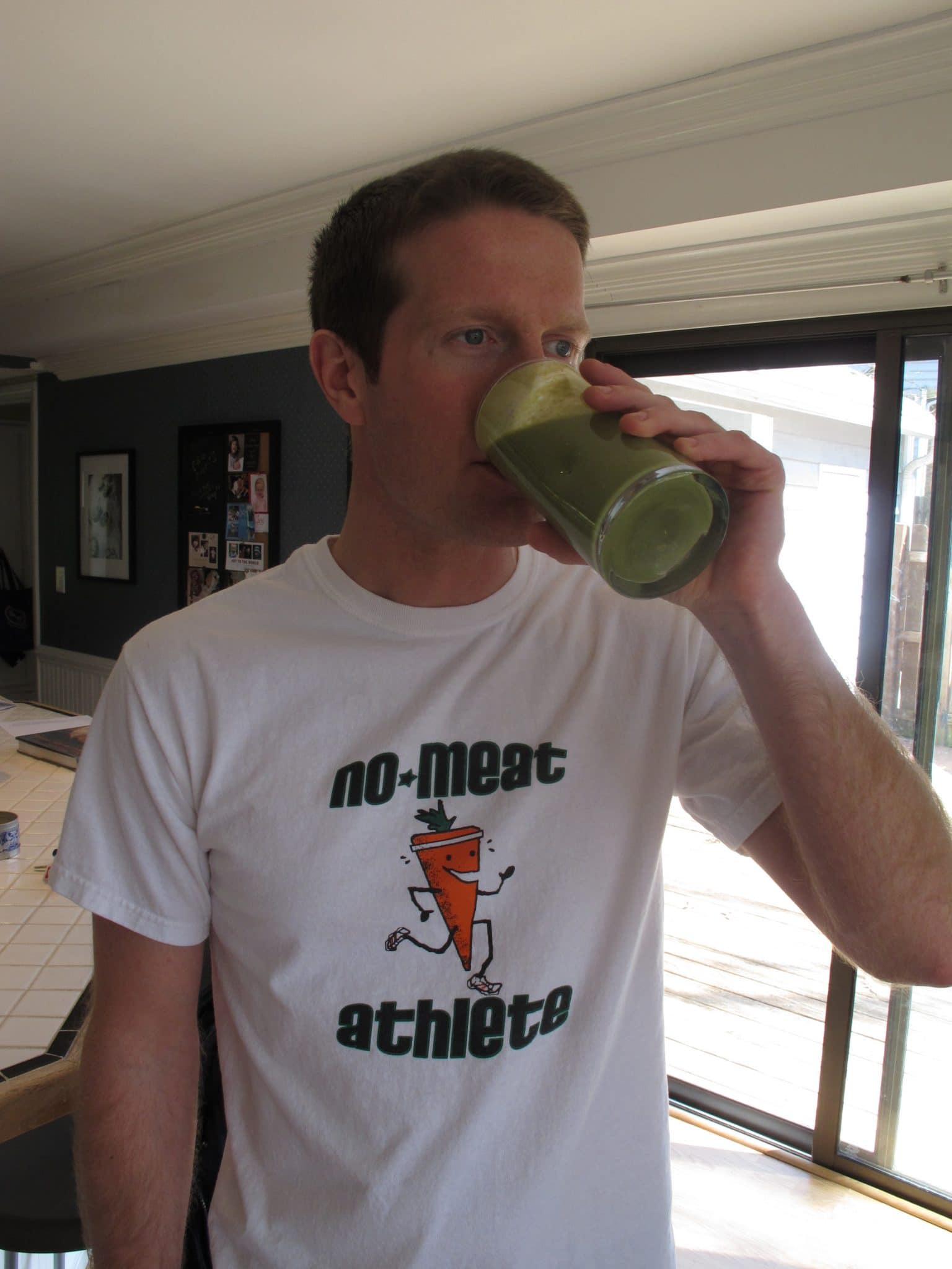 Casey drinking a green smoothie in white throwback NMA shirt