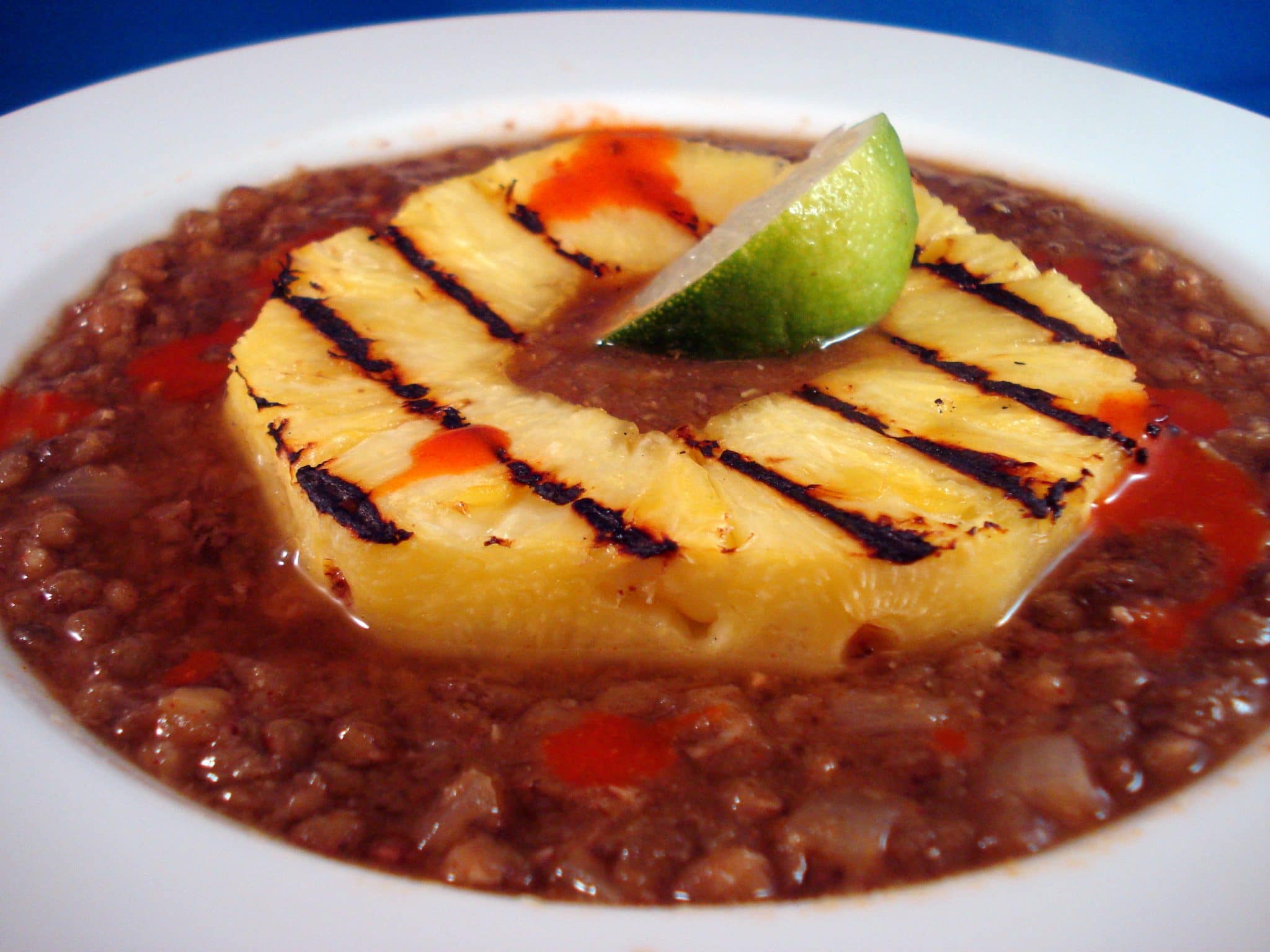 Bowl of lentil soup with grilled pineapple on top, with lime