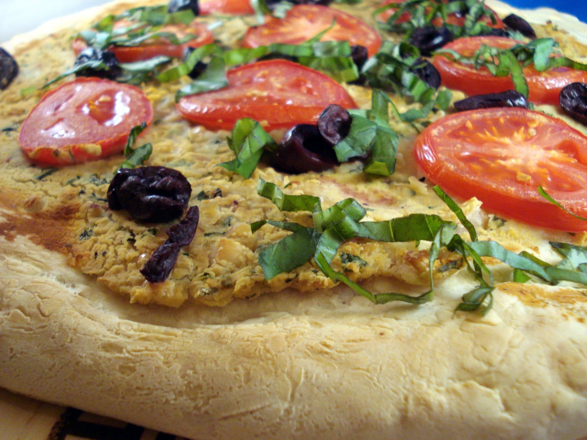 Close up of vegan pizza with homemade cashew cheese, tomatoes, and black olives