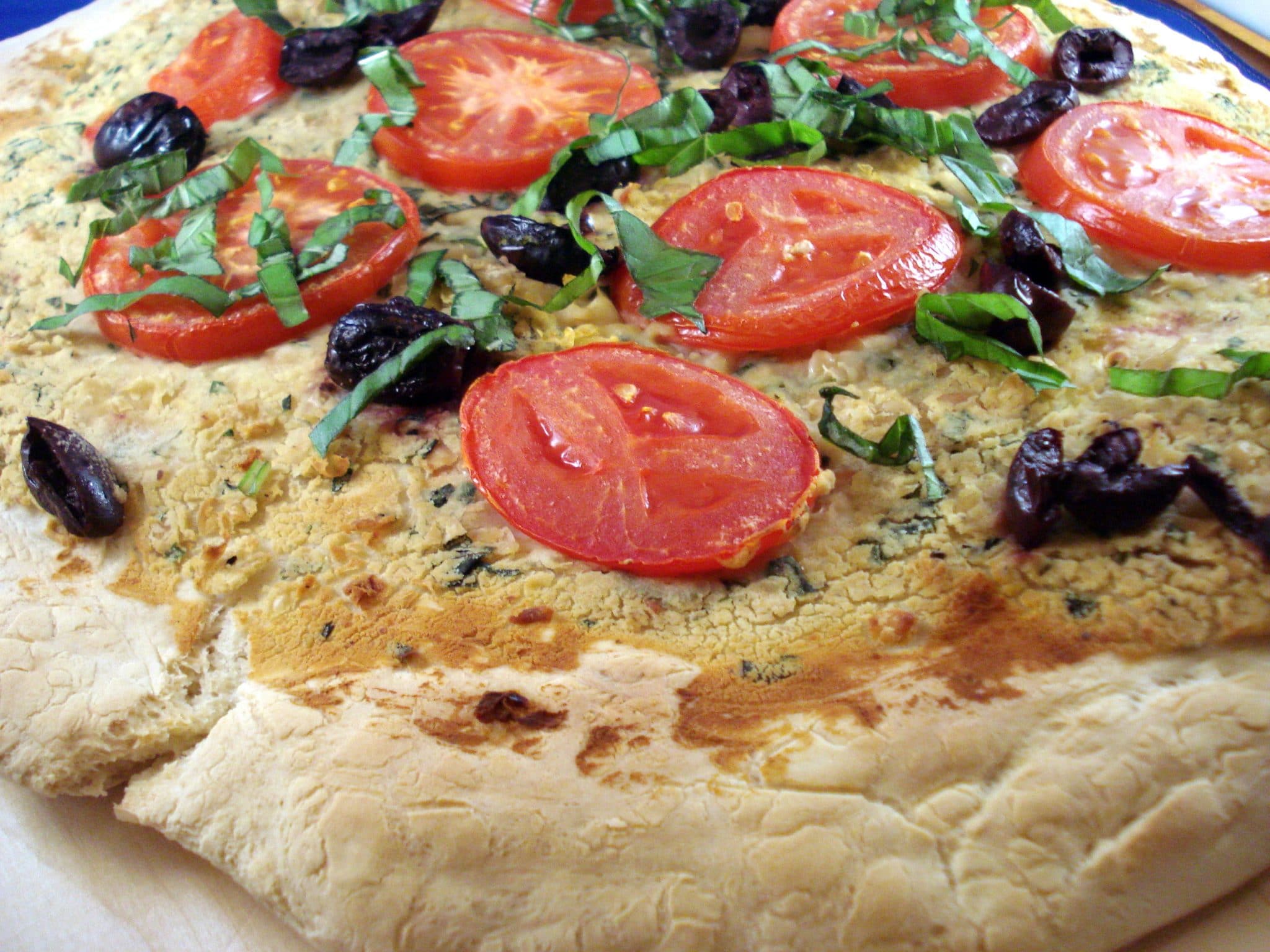 Homemade vegan pizza with tomatoes, black olives, and fresh basil