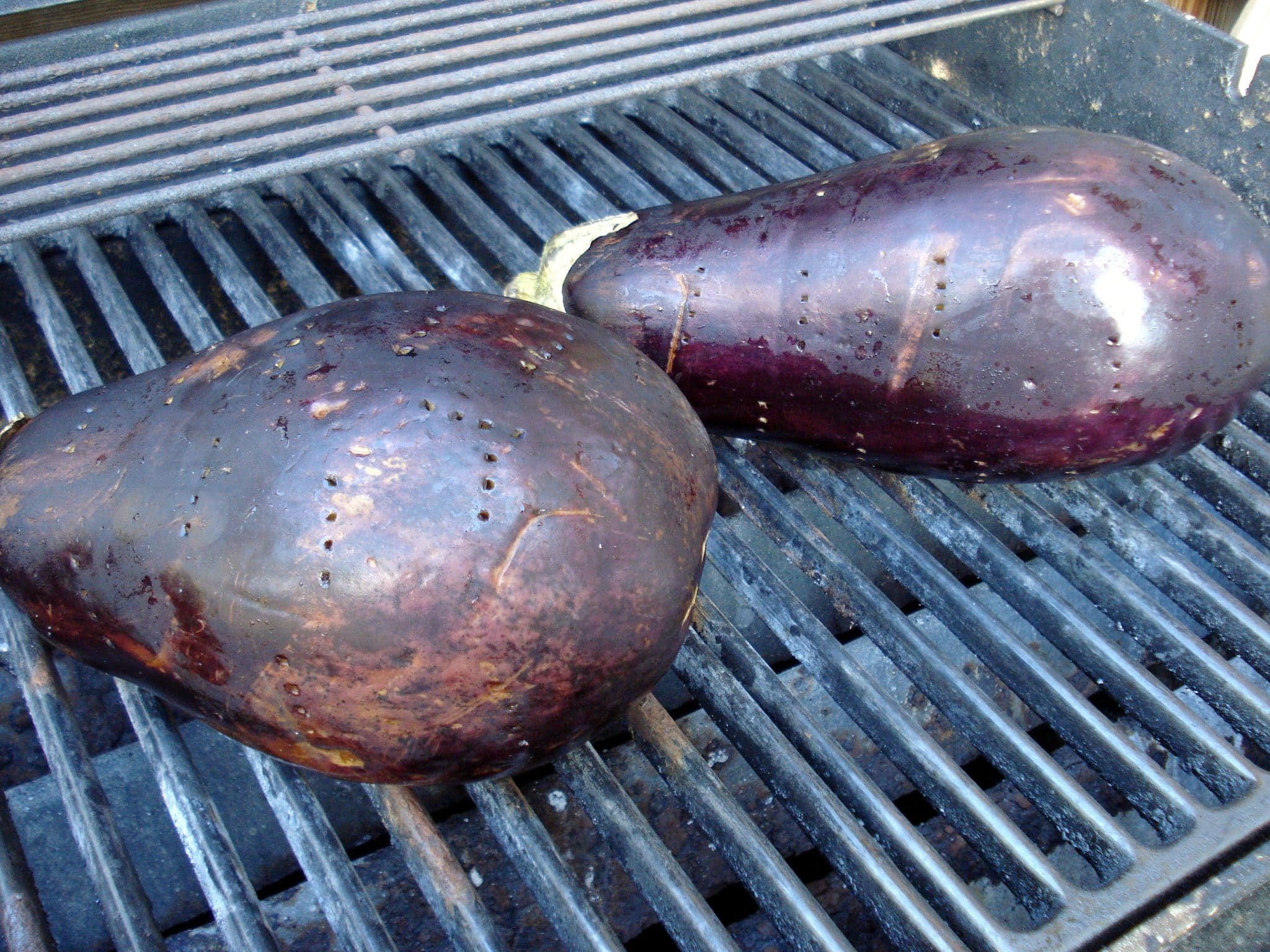 Whole eggplants roasting on the outdoor grill