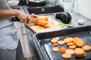 Woman slicing sweet potatoes and eggplant for baking