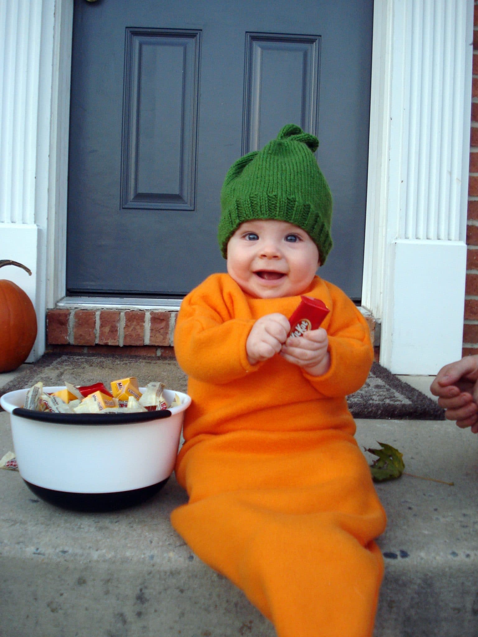Baby dressed as carrot on front porch with bowl of candy