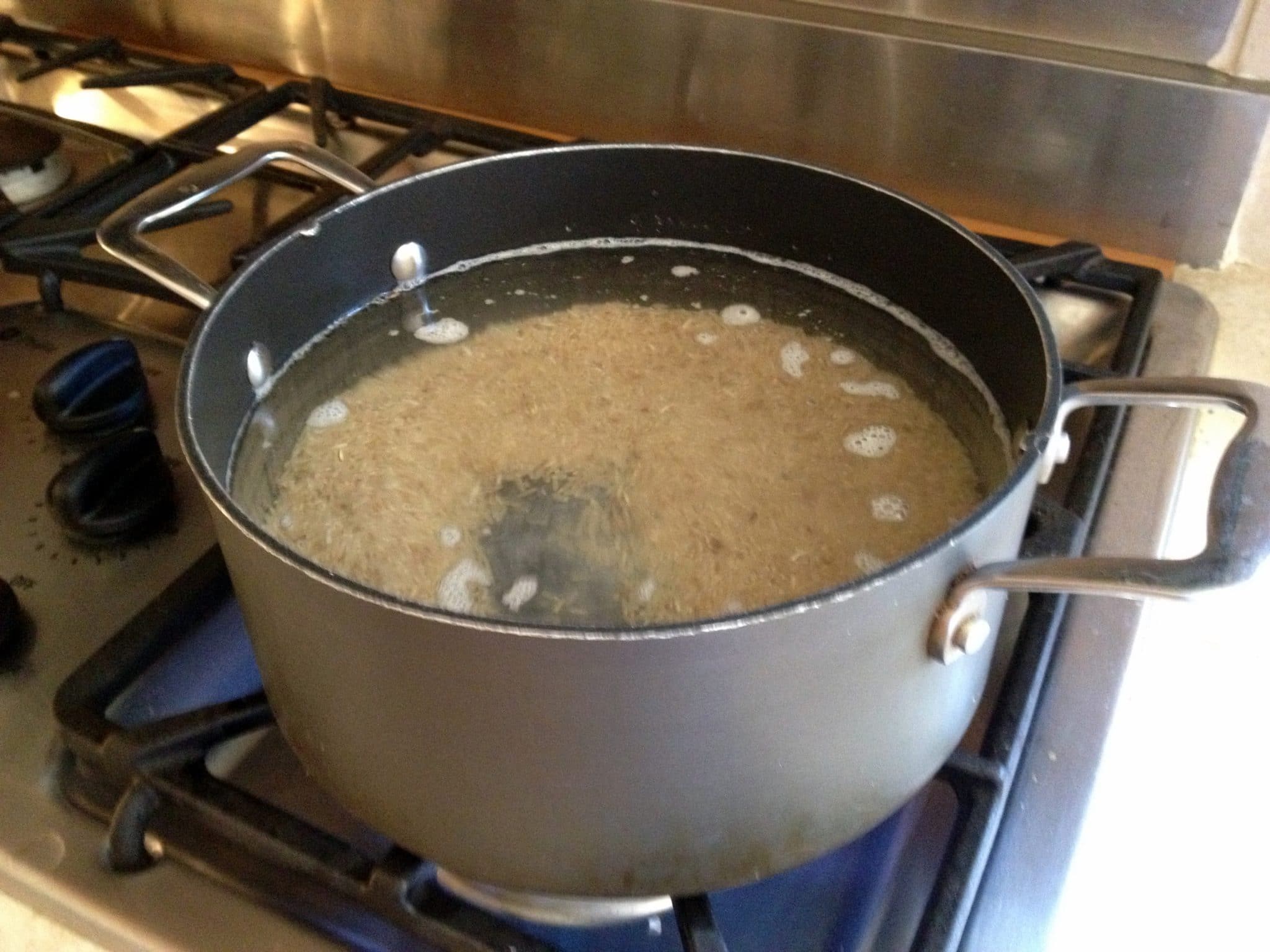 Rice, fully submerged in water in giant soup pot, being cooked as one would prepare pasta.