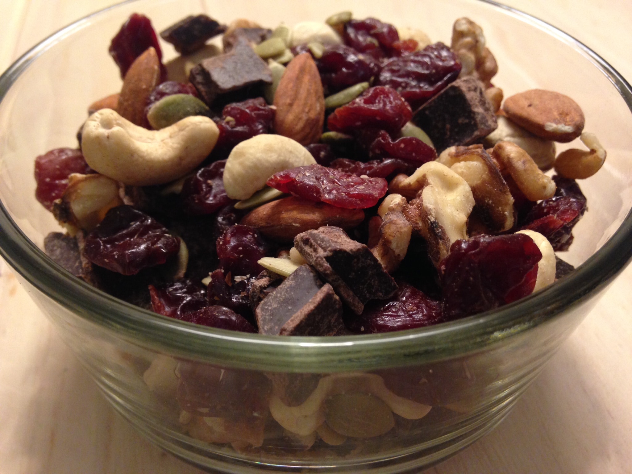 Glass bowl of trail mix: dried cranberries, dark chocolate, almonds, cashews, pumpkin seeds
