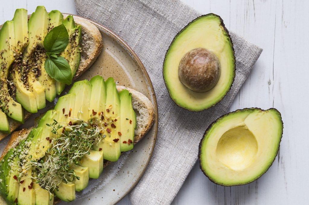 Avocado toast topped with sprouts on plate with avocado cut in half next to it