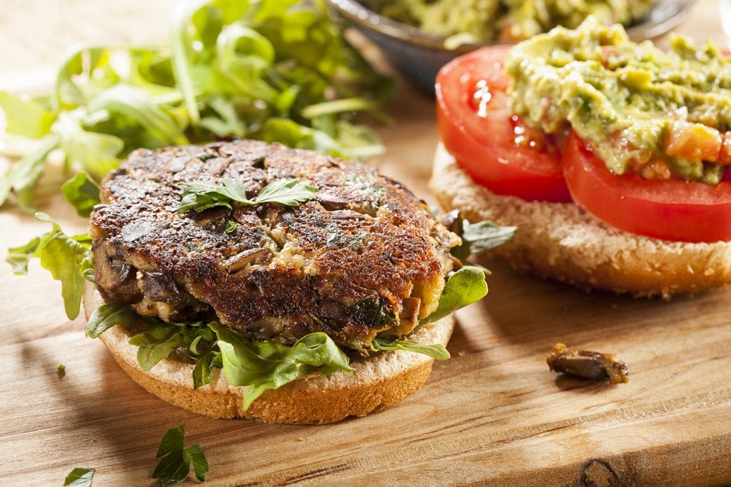 Open faced veggie burger on a bun with lettuce, tomato, and avocado.
