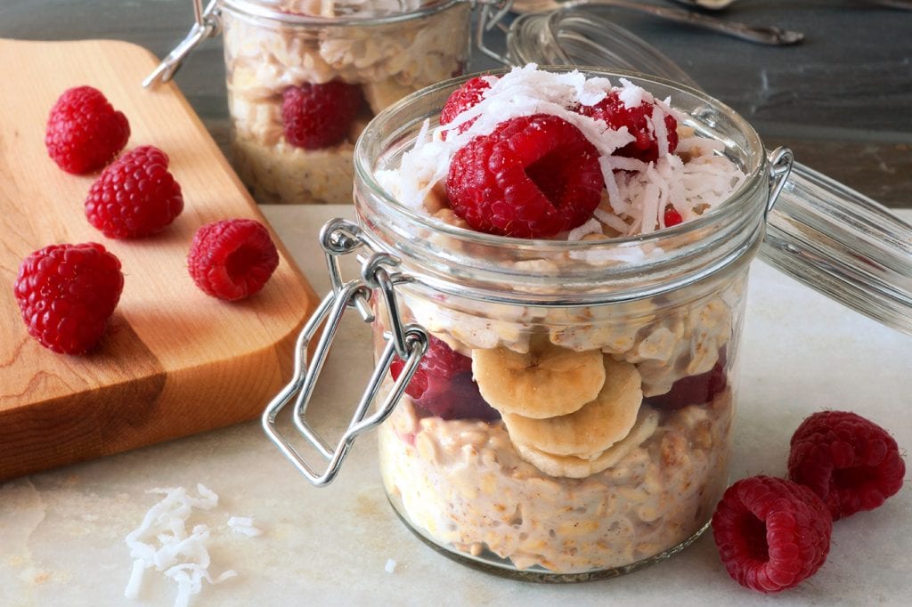 Overnight oats parfait in mini glass mason jar with raspberries, banana and coconut