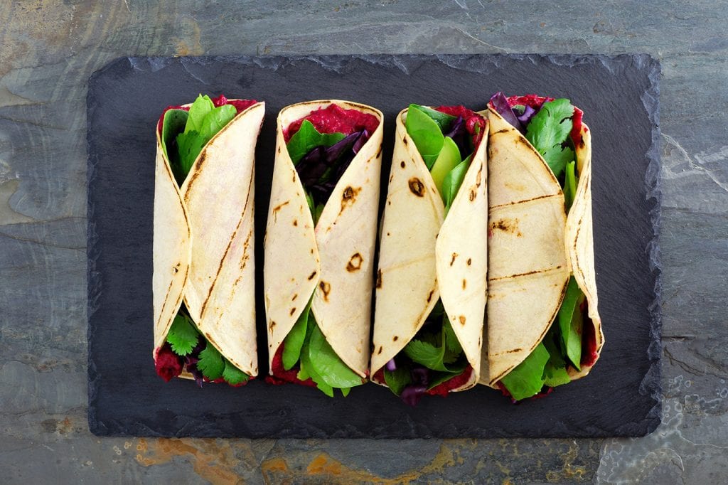 4 colorful wraps on astone plate with fresh greens and beets.